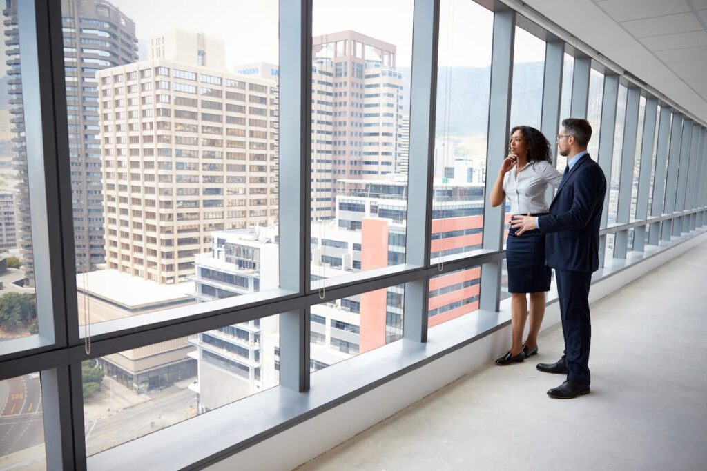 Two coworkers talking and looking out the window of a high-rise office building in a city